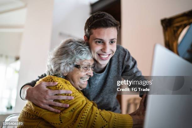 grandson and grandmother embracing and using laptop at home - good news stock pictures, royalty-free photos & images