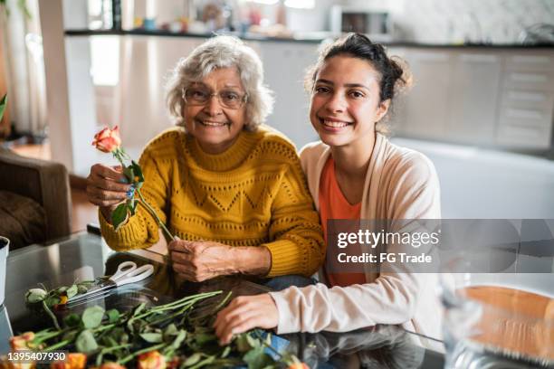 porträt einer älteren frau und ihrer enkelin, die zu hause eine blumenvase vorbereiten - teenager alter stock-fotos und bilder