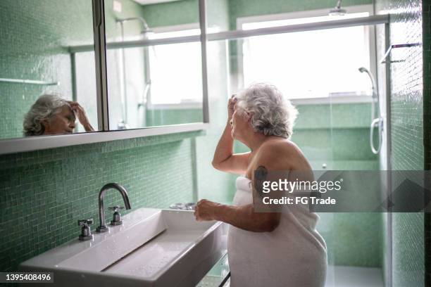 senior woman looking herself in mirror at home - old woman tattoos stock pictures, royalty-free photos & images