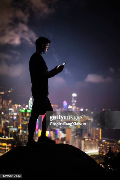 man standing and using phone to search map above cityscape at night, hong kong - lost generation stock pictures, royalty-free photos & images