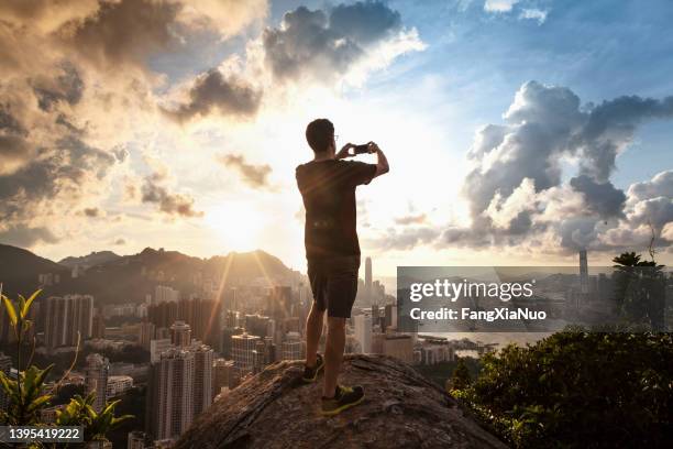 man standing on rock photographing cityscape at night, hong kong - majestic city stock pictures, royalty-free photos & images