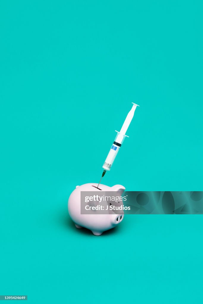 Syringe with a euro bill inserted into piggy bank