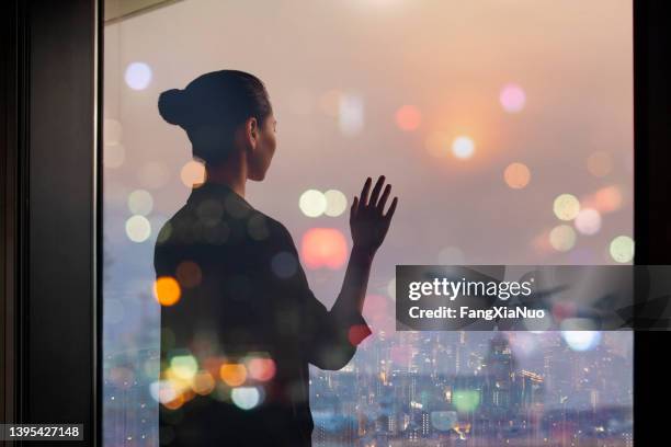 young chinese woman standing at airport terminal departure area window waving to airplane - rear view hand window stock pictures, royalty-free photos & images