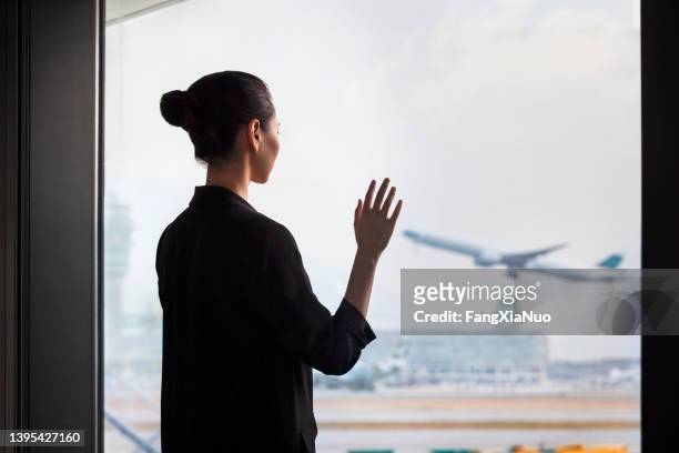 junge chinesin, die am abflugbereich des flughafenterminals steht und dem flugzeug zuwinkt - waving hands goodbye stock-fotos und bilder