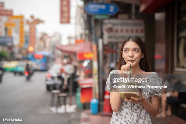 smiling young woman having a delicious and fresh coconut water on the go - daily life in bangkok photos et images de collection