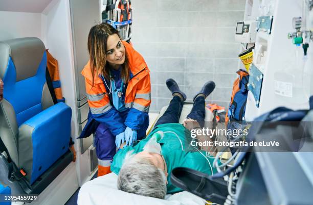 madure woman paramedic inside ambulance with a patient looking at heartbeat with an oximeter where the patient is on stretcher. - medical ambulance female stockfoto's en -beelden