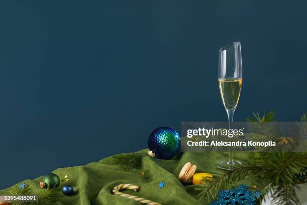 christmas ornaments, sweets and a glass of champagne on folded green velvet with solid blue background - hard liquor stock pictures, royalty-free photos & images