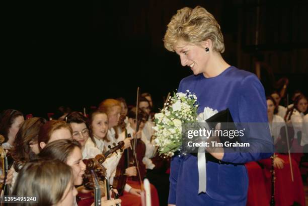 British Royal Diana, Princess of Wales wearing a blue Victor Edelstein outfit and holding a bouquet of flowers as she speaks to young musicians of...
