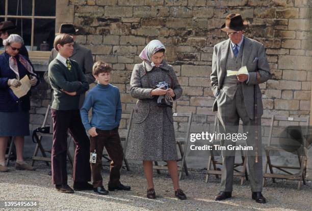 British Royal Prince Andrew stands with his arms folded, beside his cousin, David Armstrong-Jones, Viscount Linley, Queen Elizabeth II, wearing a...