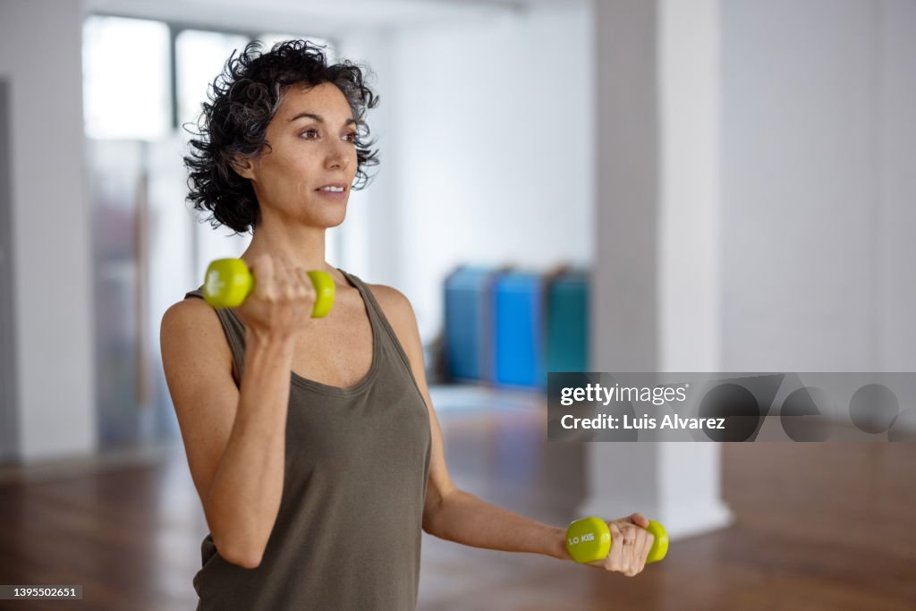 Fit mature woman doing dumbbell workout in gym