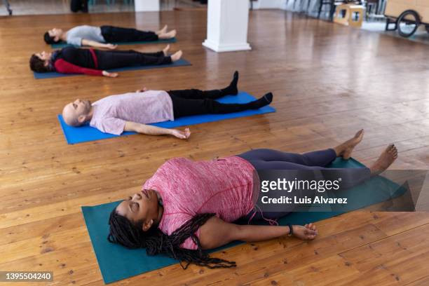 multiracial people lying on exercise mat in yoga class - black woman yoga stock pictures, royalty-free photos & images