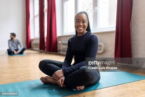 african woman yoga teacher sitting on fitness mat in class - schneidersitz stock-fotos und bilder