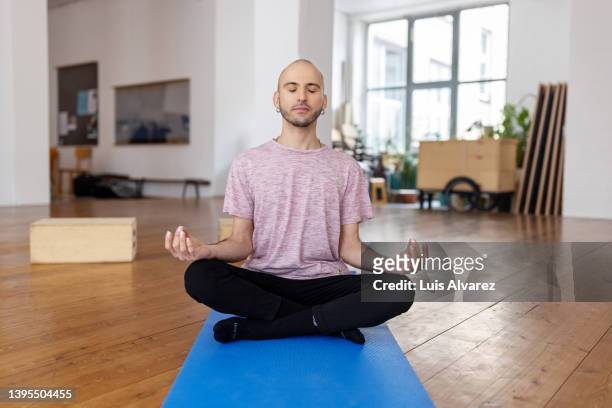 hispanic man meditating in lotus pose in yoga class - meditation concentration stock pictures, royalty-free photos & images