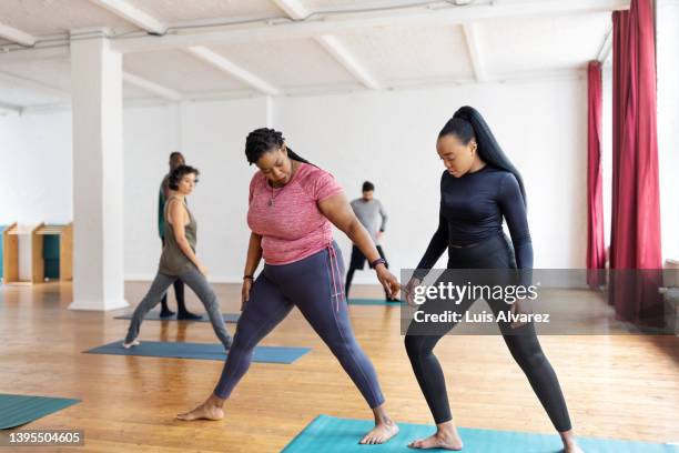fitness instructor assisting a woman doing yoga workout in health club - mature coach fotografías e imágenes de stock