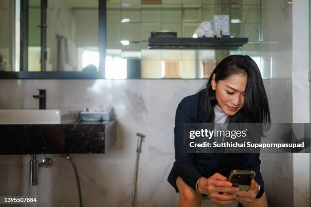 asian happy woman using smart phone while sitting on toilet seat in bathroom. - portable toilet - fotografias e filmes do acervo