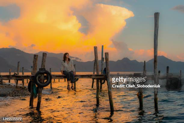 woman sitting on pier on atitlan lake in guatemala at sunset - panajachel stock pictures, royalty-free photos & images