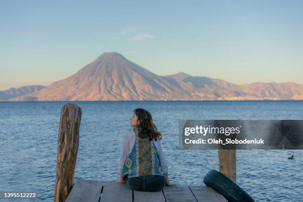 woman sitting on pier on atitlan lake in guatemala at sunset - lake atitlan stock pictures, royalty-free photos & images