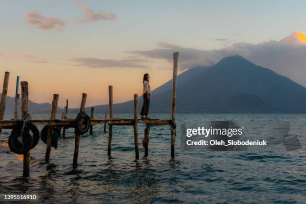 woman standing on pier on atitlan lake in guatemala at sunset - volcán de fuego guatemala stock pictures, royalty-free photos & images