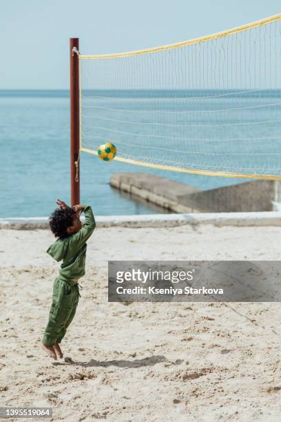 a little dark-skinned boy with an afro hairstyle plays volleyball on a sandy beach against the background of the sea - volleyball player photos et images de collection