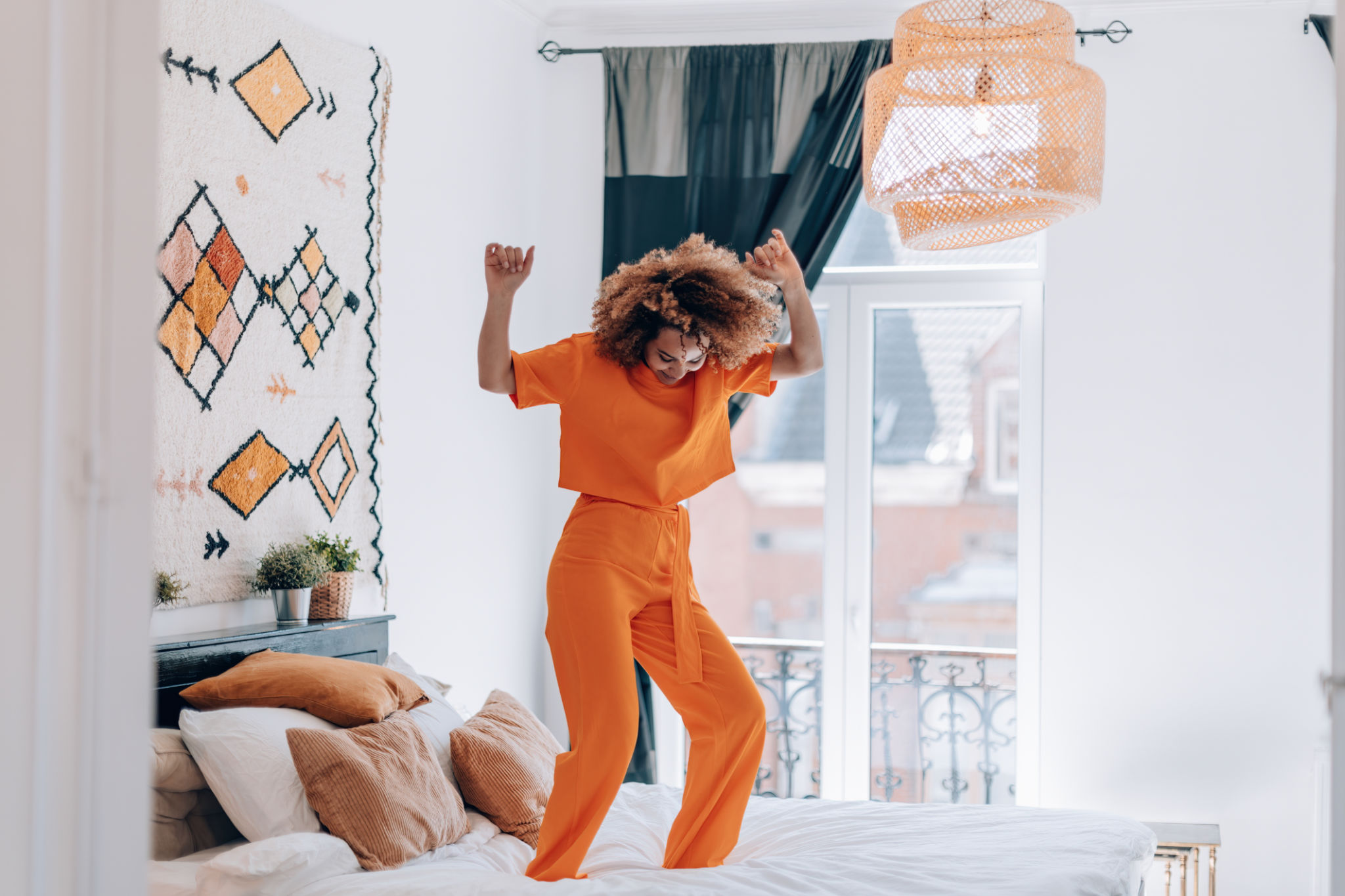 happy young woman in orange outfit dancing on bed happy young woman in orange outfit dancing on bed