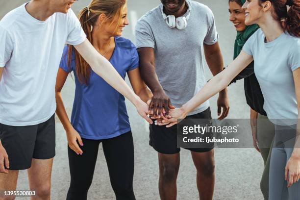 multi-ethnical group of young adult runners cheering and high fiving after a good run outdoors - coach cheering stock pictures, royalty-free photos & images