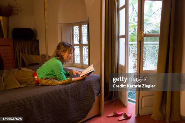 woman lying on bed, reading a book - red house slippers stock pictures, royalty-free photos & images