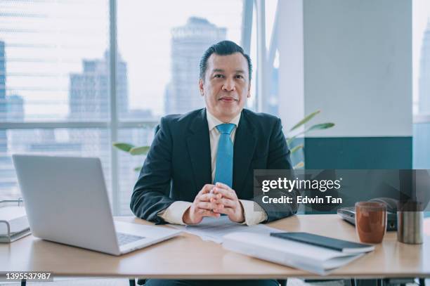 asian malay man ceo senior management looking at camera smiling at his desk in office - serious interview stock pictures, royalty-free photos & images