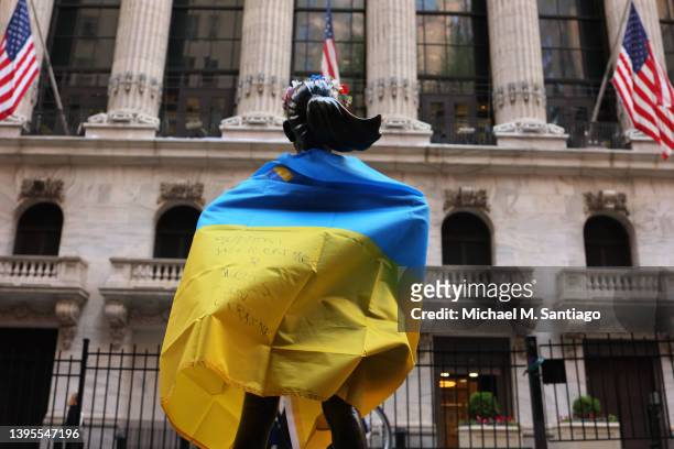 The Fearless Girl statue is seen draped in the flag of Ukraine in front of the New York Stock Exchange on May 05, 2022 in New York City. Stocks...