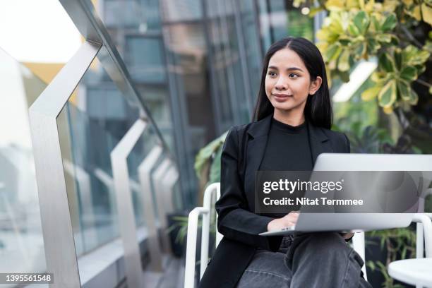 working remotely for the new generation of creative entrepreneurs. young asian business woman working on laptop while looking away, sitting at bar rooftop hotel. - investment solutions stock pictures, royalty-free photos & images