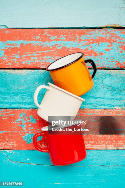 still life of a stack of three enamel cups on turquoise and red wooden background - still life stockfoto's en -beelden