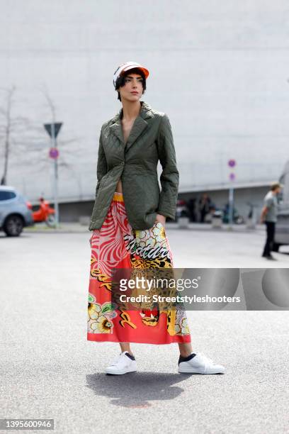 Model and artist Zoe Helali wearing an olive green jacket with a pink and silver crystal smiley face by Miss Goodlife, a multicolored maxi skirt with...