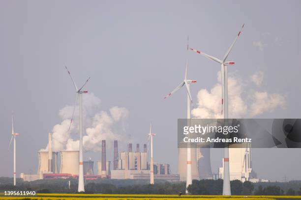 Steam rises from cooling towers of the Neurath coal-fired power plant as wind turbines spin over a field of rapeseed on May 05, 2022 near Bedburg,...