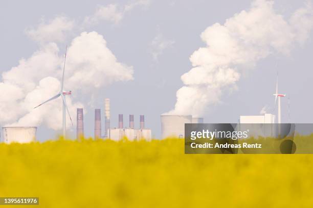 Steam rises from cooling towers of the Neurath coal-fired power plant as wind turbines spin over a field of rapeseed on May 05, 2022 near Bedburg,...