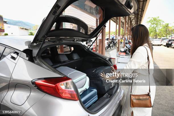 asian woman loading luggage into rental car - car rental stockfoto's en -beelden