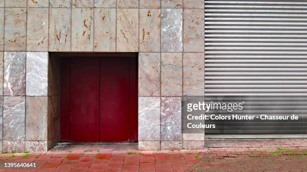 pink marble empty wall with red double door, gray metal roller shutter and red cobblestone sidewalk in brussels - iron roll stockfoto's en -beelden