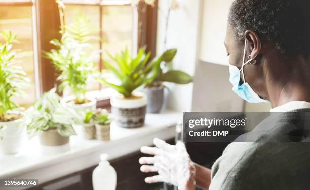 a mature woman washing her hands in the kitchen sink. senior woman wearing a face mask and cleaning her hands at home - infection control stock pictures, royalty-free photos & images