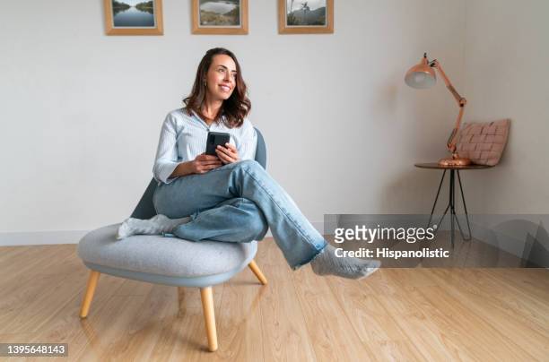 mujer relajándose en casa y enviando mensajes de texto en su teléfono celular - cuarentena fotografías e imágenes de stock