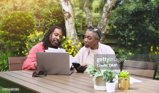 a senior couple using a laptop and going over paperwork in the garden at home. mature man and woman discussing finance while browsing online with a computer - erfenis stockfoto's en -beelden