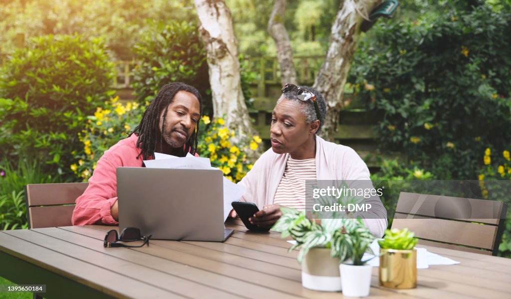 A senior couple using a laptop and going over paperwork in the garden at home. Mature man and woman discussing finance while browsing online with a computer