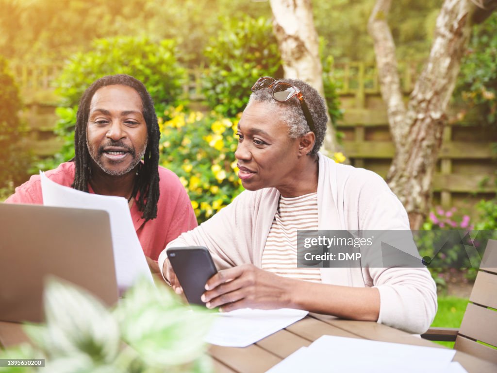A senior couple using a laptop and going over paperwork in the garden at home. Mature man and woman discussing finance while browsing online with a computer