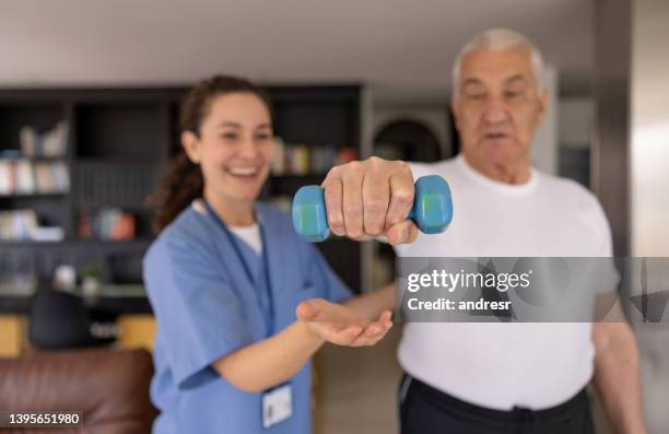 happy physical therapist helping a senior man with his recovery at home - clean house stockfoto's en -beelden