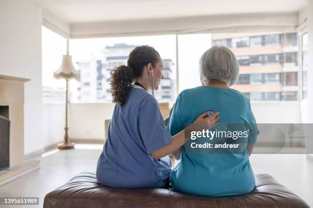 cuidadora a domicilio escuchando el corazón de una mujer mayor - residencia para enfermos terminales fotografías e imágenes de stock