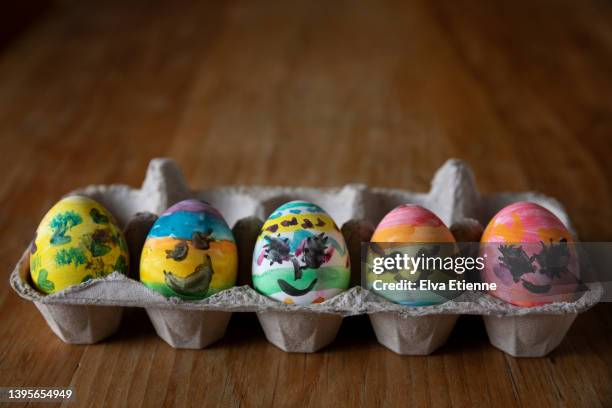 hens eggs freshly painted with multicoloured paints by a child and left to dry in a cardboard egg box on a wooden dining table. - anthropomorphic stock pictures, royalty-free photos & images