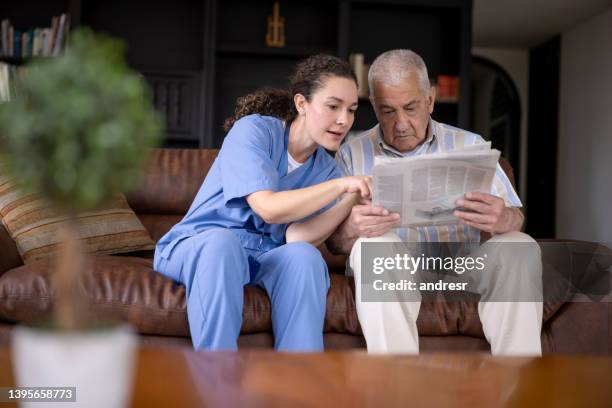 senior man reading the newspaper at home with assistance of his caregiver - hospitium stockfoto's en -beelden