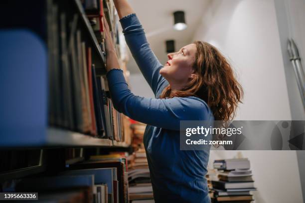 beautiful university student reaching books on upper shelves in the library - reaching higher stock pictures, royalty-free photos & images