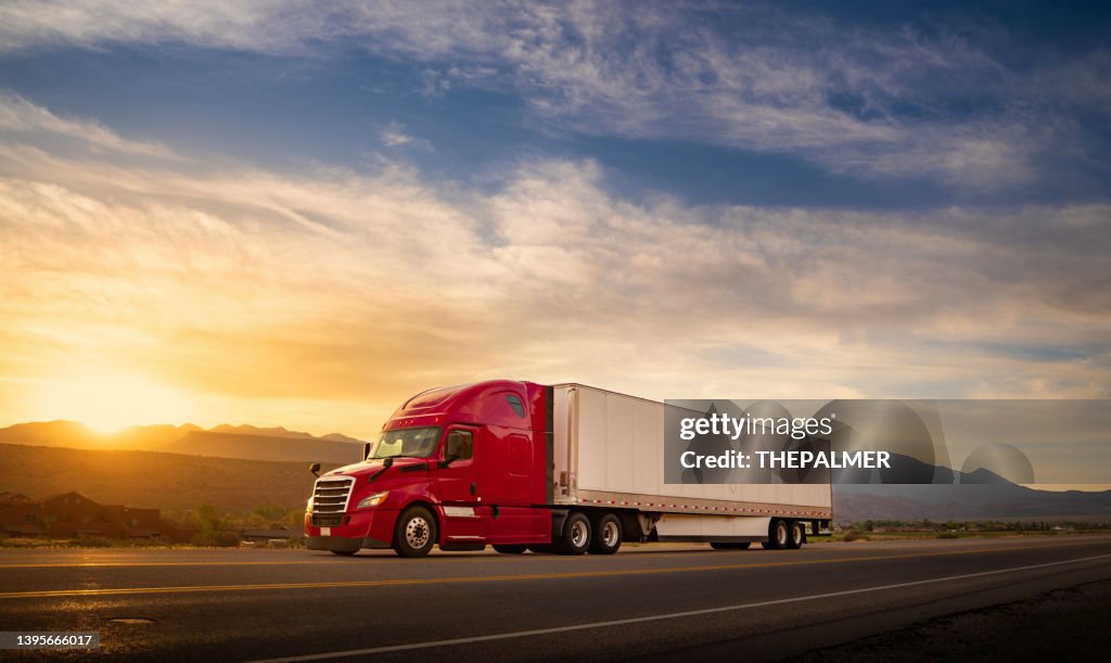 Red and white semi-truck speeding at sunrise on a single lane road USA