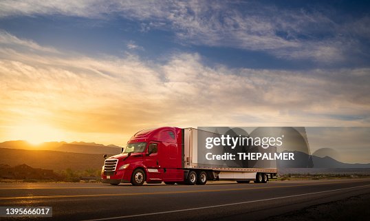 Red and white semi-truck speeding at sunrise on a single lane road USA Red and white semi-truck speeding at sunrise on a single lane road USA
