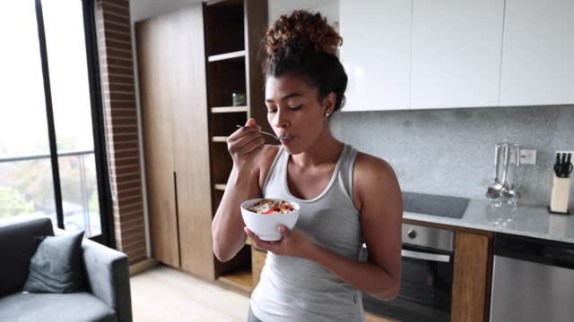 Beautiful black young woman enjoying a delicious cereal after her morning workout at home