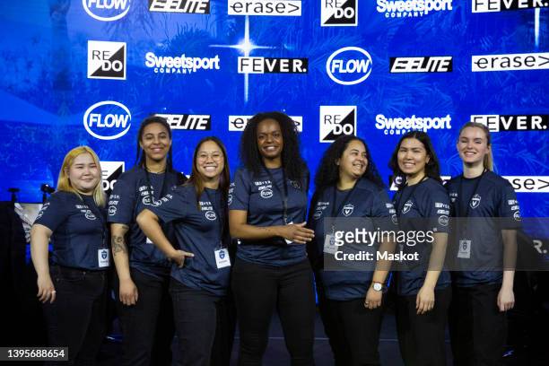 portrait of smiling female coach and gamers standing against sponsor logos at esports tournament - 贊助者 個照片及圖片檔