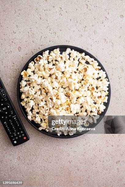 close-up of salted popcorn on a black plate and remote control on concrete background, high angle view. copy space. - popcorn photos et images de collection